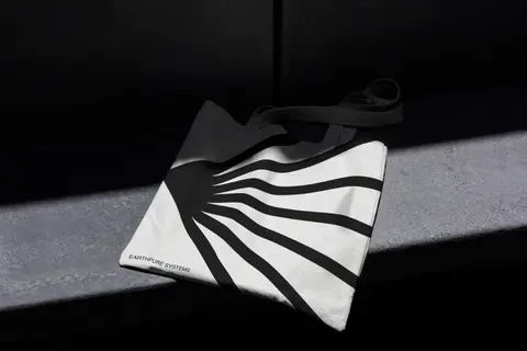 Tote bag with a black-and-white sunburst mark, in hard shadow.