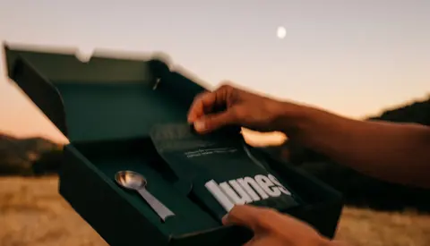 An open green Lunes box held in two hands at dusk.