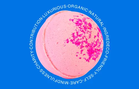 A pink bath bomb ringed with a circle of words such as luxurious, organic and natural, on bright blue.