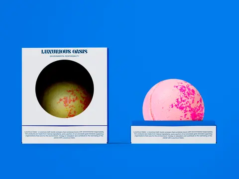 A white Oasis box with a round window beside a pink bath bomb on bright blue.