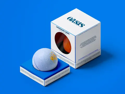 A white cube box with a round window and a pale bath bomb on a blue plinth.