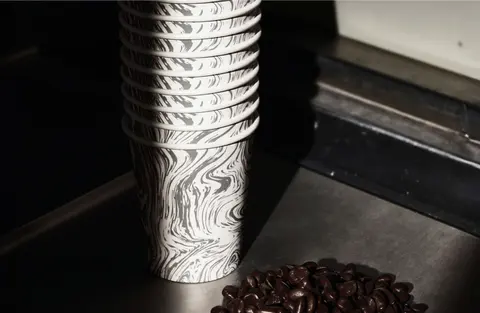 A stack of marbled paper cups beside coffee beans, in a dark scene.