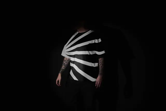 A person in the dark wears a black t-shirt with a large white fan-shaped mark.