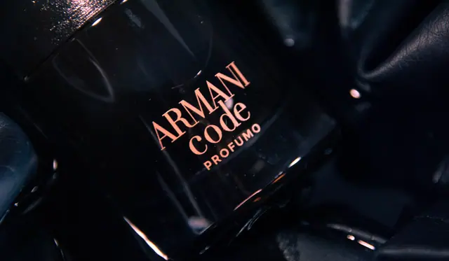 Dark moody close-up of a black perfume bottle with copper lettering lying on black leather.