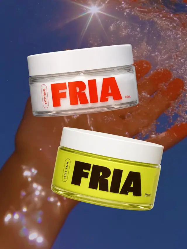 Two body balm jars, one white and red, one lime and brown, held up in sunlit water.