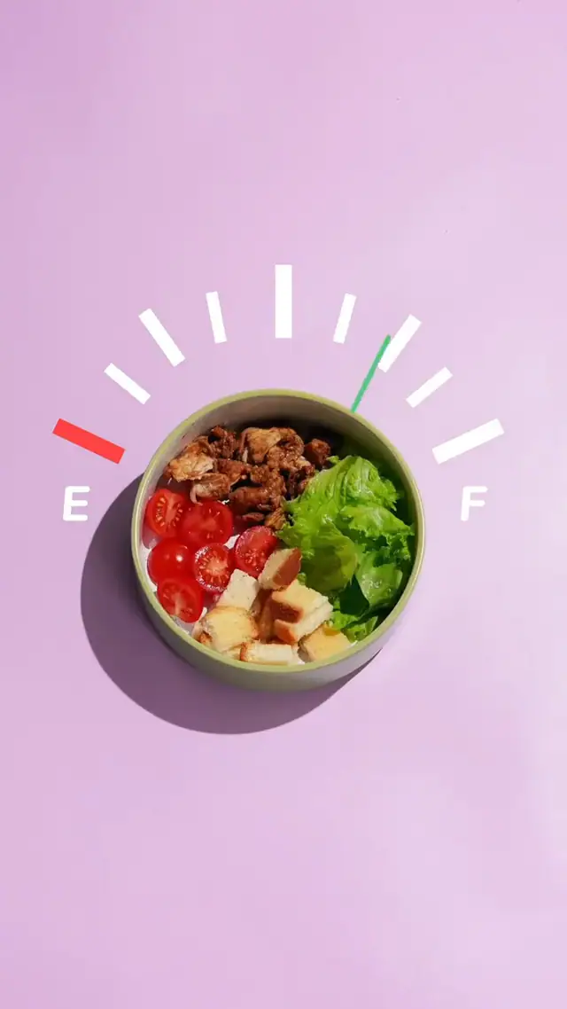 A bowl on a pink ground fills with salad as a fuel gauge needle swings from empty to full.